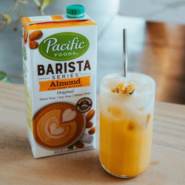 Pacific Foods Barista Series Almond Original Beverage carton next to a glass of iced coffee with a straw. A dairy-free, plant-based alternative designed for steaming, frothing, and blending into coffee drinks.