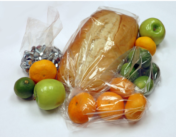 Clear plastic bags filled with various food items, including a loaf of bread, oranges, limes, green apples, and wrapped chocolates, demonstrating their versatility for food storage.
