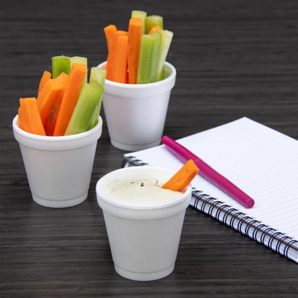 Image of three 4 oz white EPS foam cups filled with celery and carrot sticks, with one cup containing a dipping sauce. Ideal for serving small portions, snacks, and condiments in foodservice settings.
