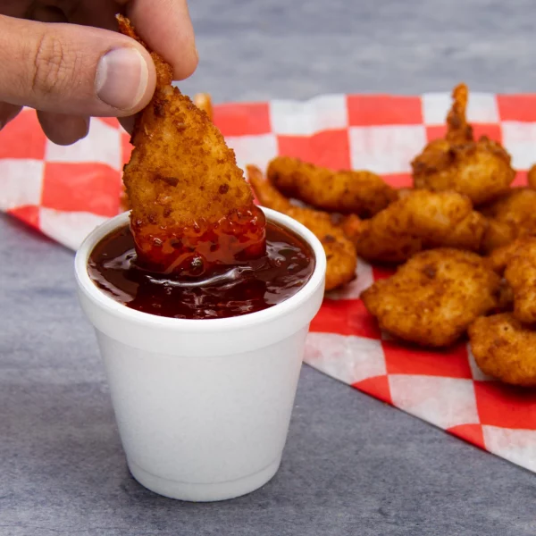 Image of a 4 oz white EPS foam cup filled with dipping sauce, with a hand dipping a crispy fried appetizer. Ideal for serving sauces, condiments, and small portions in restaurants and foodservice settings.